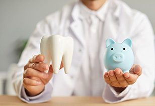 A dentist holding up a model tooth and a blue piggy bank