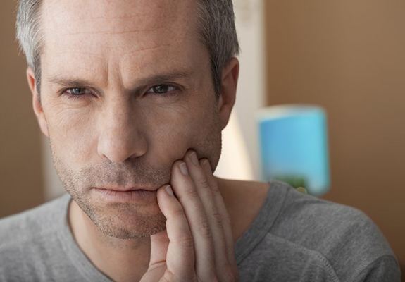 older man in gray shirt holding his mouth in pain 