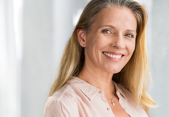 A middle-aged woman wearing a pink blouse and smiling after completing treatment for a smile makeover