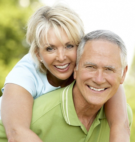 Older man and woman smiling after replacing missing teeth