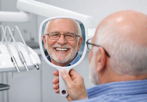 Happy senior patient looking at his smile in mirror