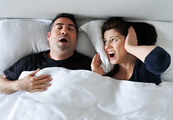 Woman covering ears next to snoring man