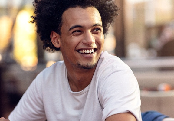 A young male wearing a white t-shirt and smiling after undergoing a smile makeover