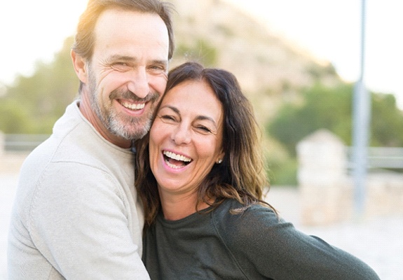 A middle-aged couple laughing, hugging, and smiling while standing outdoors