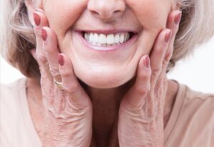 Senior woman holding face smiling with dentures.